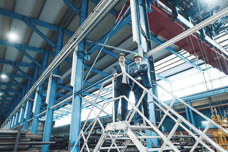 Dos responsables recorren una nave industrial desde una plataforma de acceso. La presunción de conformidad vincula a las autoridades de control; no libera al fabricante ni al usuario de sus obligaciones propias. Imagen corporativa tec.nicum.